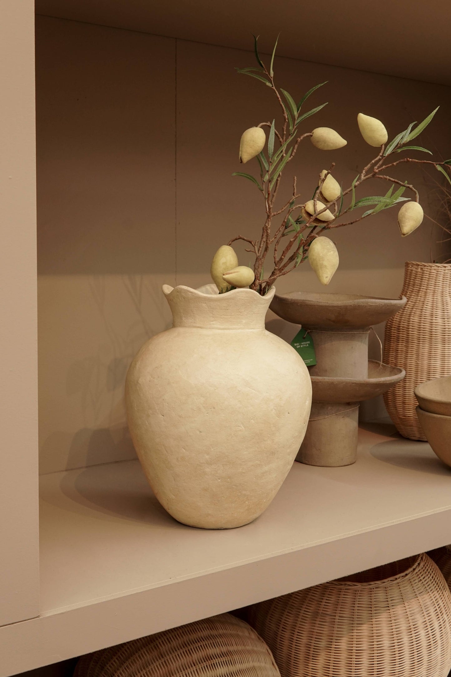 Handgefertigte terrakotta-vase „Mara“ in warmem Gelb-Beige mit Zweigen und dekorativen Elementen auf einem Regal.